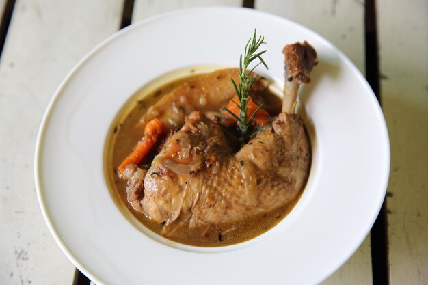 Coq au vin, in Rotwein gedünstetes Hühnchen mit Karotten und Kartoffeln auf Holzhintergrund, französische Speisen