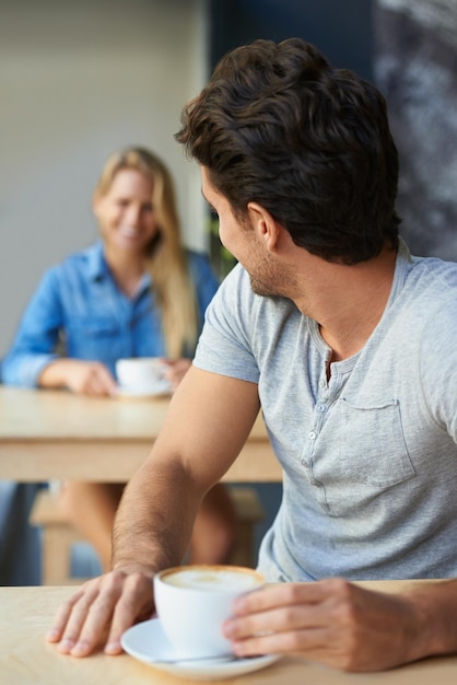 Coqueteando desde lejos Un joven en una cafetería mirando hacia atrás para ver a la chica detrás de él