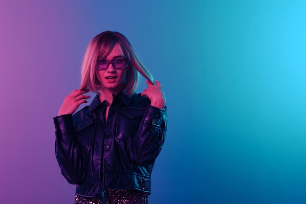 Coqueteando sexy adorable hermosa mujer rubia en chaqueta de cuero vestido brillante gafas de sol de moda posando aisladas en fondo de estudio de luz de color rosa azul fiesta de neón concepto Cyberpunk espacio de copia