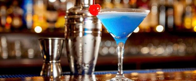 Foto coquetel azul em um copo de martini com uma cereja, um bar e um batedor de coquetel ao fundo