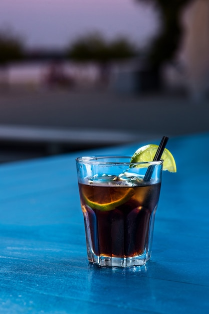 Coquetel casual de rum cola com cubos de gelo e limão no fundo do carrinho de bar de verão