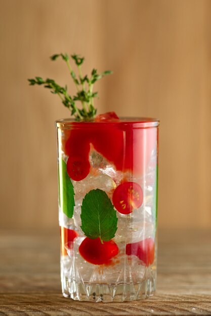 Foto coquetel com vodka, tomate, hortelã e cubos de gelo na mesa de madeira