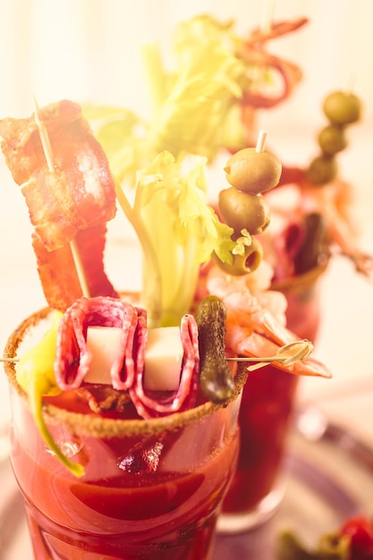 Foto coquetel de bloody mary decorado com palitos de aipo, azeitonas e tiras de bacon.