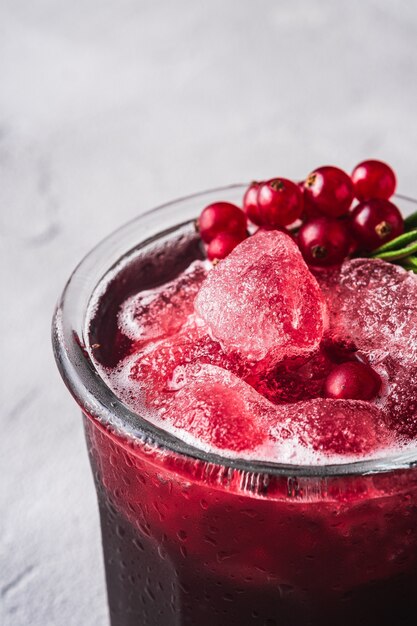 Coquetel de frutas frescas em um copo, bebida refrescante de frutas vermelhas com folha de alecrim na mesa de pedra de concreto, macro de visão angular