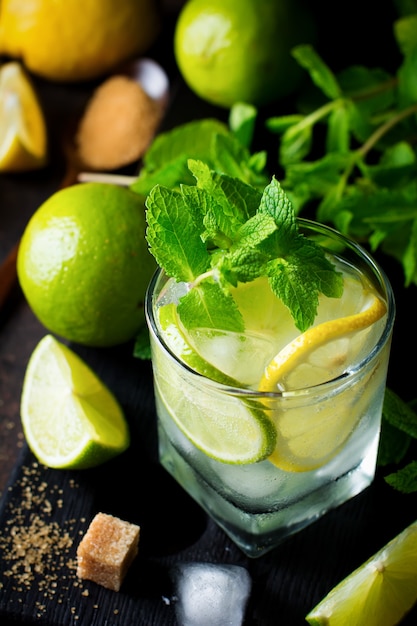 Coquetel de mojito em copo com limão, hortelã fresca e gelo no escuro.