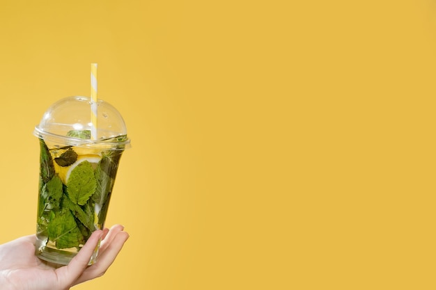 Coquetel de mojito em um copo de plástico com um tubo em um fundo amarelo. bebida fresca no verão para levar. lugar para texto.