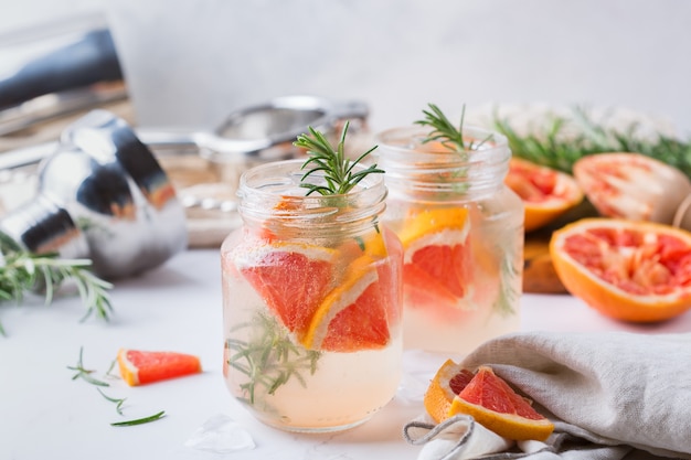 Coquetel de seltzer duro com toranja, alecrim e gelo em uma mesa. Bebida refrescante de verão, bebida em uma mesa branca