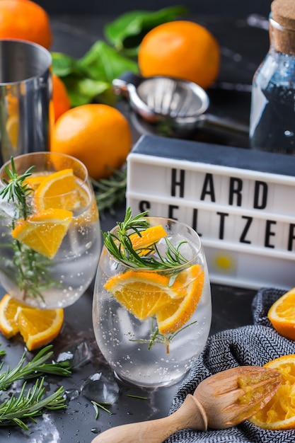 Coquetel de seltzer forte com laranja, alecrim e gelo em uma mesa. Bebida refrescante de verão, bebida em uma mesa preta