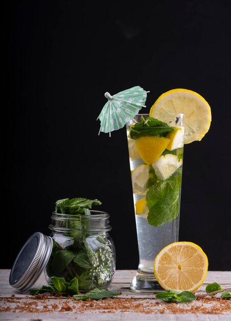 Coquetel de suco de limão com gelo e hortelã acompanhado de um frasco de vidro com hortelã em uma base de madeira