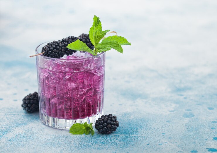 Foto coquetel de verão refrescante com amora em copo de cristal com cubos de gelo e hortelã sobre fundo azul. mistura de refrigerante e álcool. espaço para texto