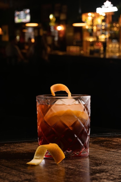 Coquetel negroni com gelo redondo na mesa de madeira com fundo de pub turva