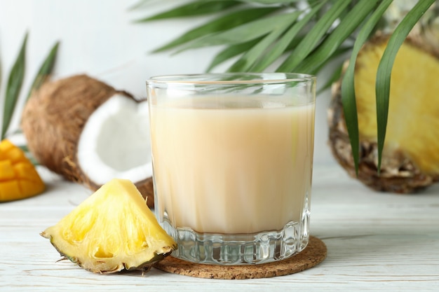 Coquetel Pina Colada e ingredientes na mesa de madeira branca.