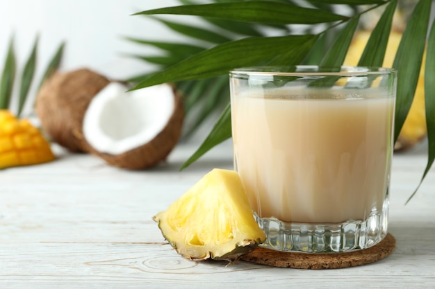 Coquetel pina colada e ingredientes na mesa de madeira branca.