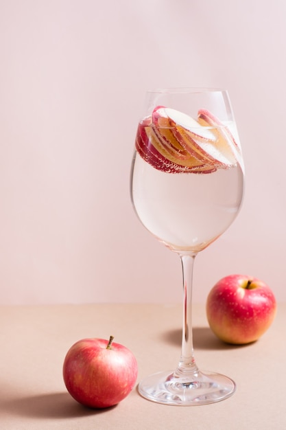 Coquetel refrescante de pedaços de maçã e água mineral em um copo com fundo rosa. Bebida de bem-estar desintoxicante. Visão vertical