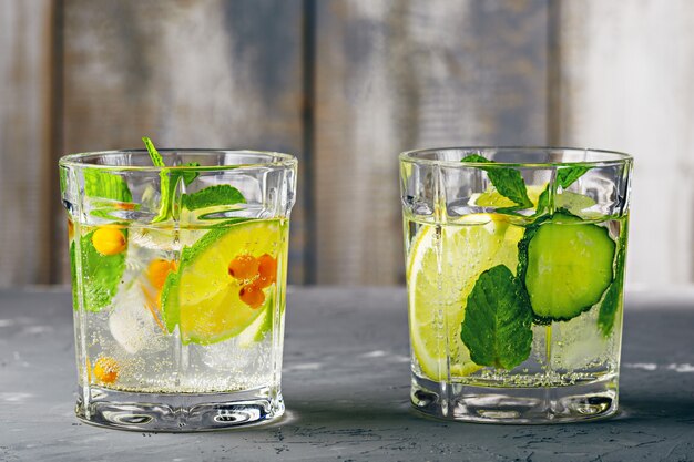 Coquetel saudável e refrescante com limão, lima, espinheiro, pepino e hortelã na mesa de madeira cinza