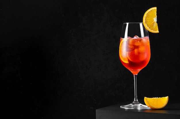 Coquetel Spritz em taça de vinho com gelo e uma fatia de laranja em fundo escuro