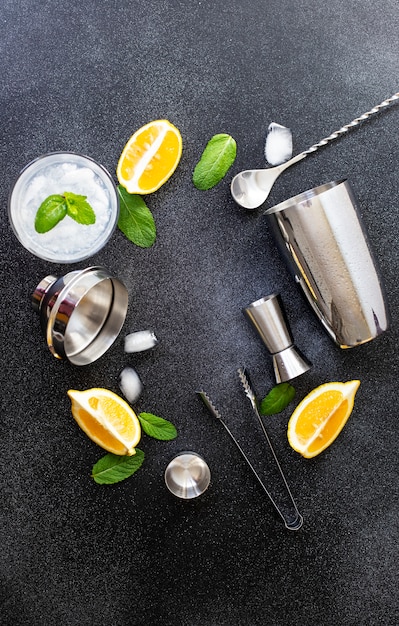 Coqueteleira e ferramentas de bar. ingredientes para um coquetel alcoólico frio. mojito cocktail. limão, hortelã, gelo, rum. vista superior, vertical, fundo preto, copie o espaço