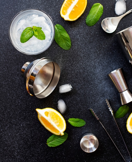 Coqueteleira e ferramentas de bar. Ingredientes para um coquetel alcoólico frio. Mojito Cocktail. Limão, hortelã, gelo, rum. Vista superior, vertical, fundo preto, copie o espaço