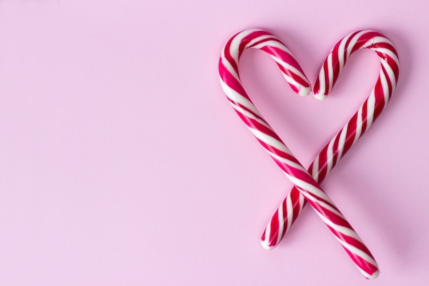 Coração de caramelo em bastões brancos em uma faixa vermelha em uma rosa