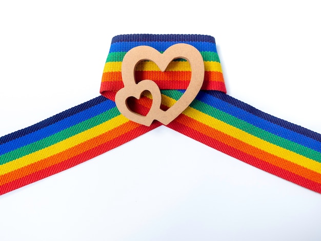 Foto coração de casal de madeira na fita de listra do arco-íris, isolada no fundo branco. conceito lgbt com cores do orgulho e faixa da bandeira do arco-íris. fundo de banner lgbt.