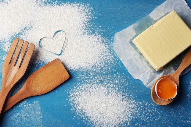 Coração de farinha e utensílios de cozinha de madeira sobre fundo azul