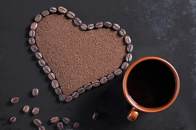 Coração de feijão e xícara de café marrom na vista superior de fundo de metal preto antigo