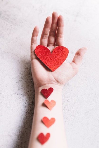 Coração de glitter vermelho em forma de papelão na mão e pequenas corações na superfície branca. conceito de amor e dia dos namorados.
