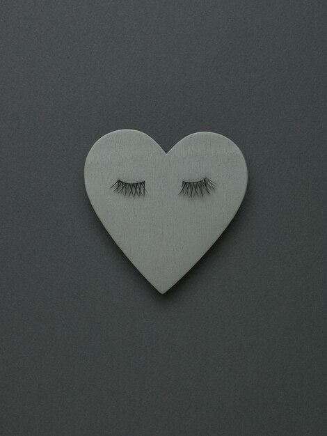 Coração de madeira cinza com cílios em um fundo cinza escuro. O conceito de Dia dos Namorados. Postura plana.