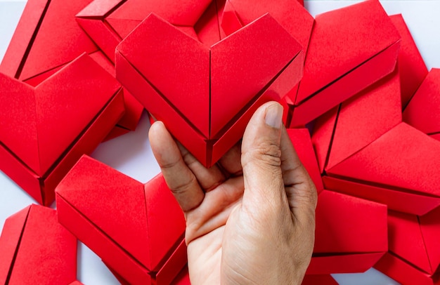 Coração de papelmãos segurando o coração de origami dobrado fundo branco garotinhos mão segurando um coração vermelho