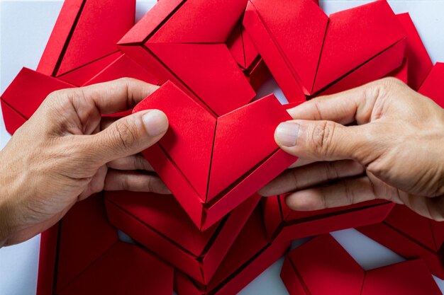 coração de papelMãos segurando o coração de origami dobrado fundo branco garotinhos mão segurando um coração vermelho