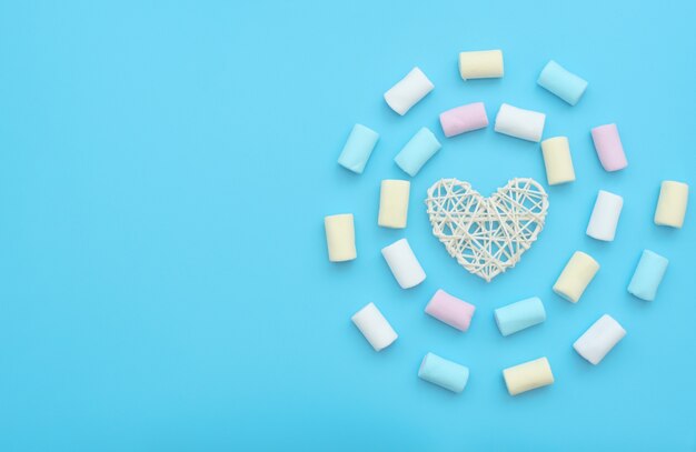 Coração de rattan branco e deliciosos marshmallows em fundo azul