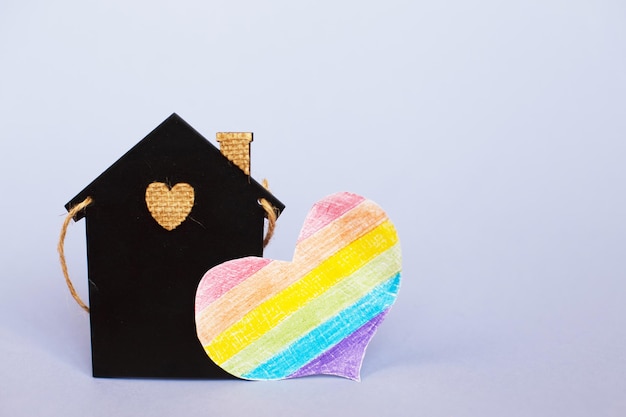 Coração em forma de bandeira lgbt ao lado de uma casa de brinquedos em miniatura.