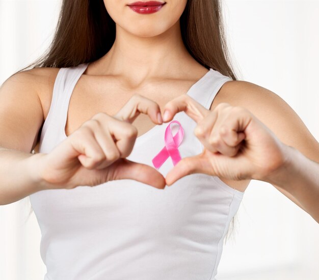 Foto coração emoldurando os dedos no peito da mulher com distintivo rosa para apoiar a causa do câncer de mama