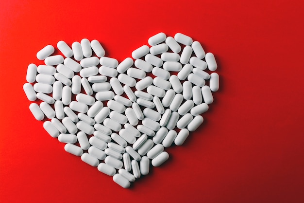 Coração feito de comprimidos brancos sobre fundo vermelho, medicamentos para doenças cardíacas