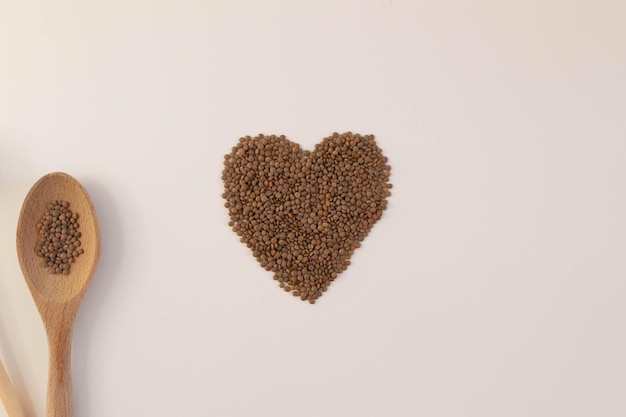 Coração feito de lentilhas cruas em um fundo branco com utensílios de cozinha