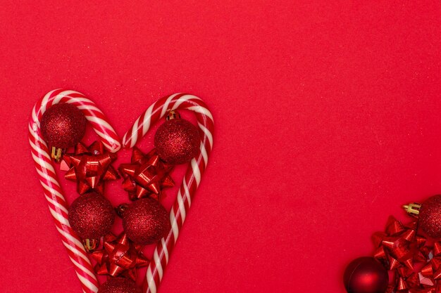 Coração flatlay de natal forrado com pirulitos de natal e decorado com brinquedos de árvore de natal.