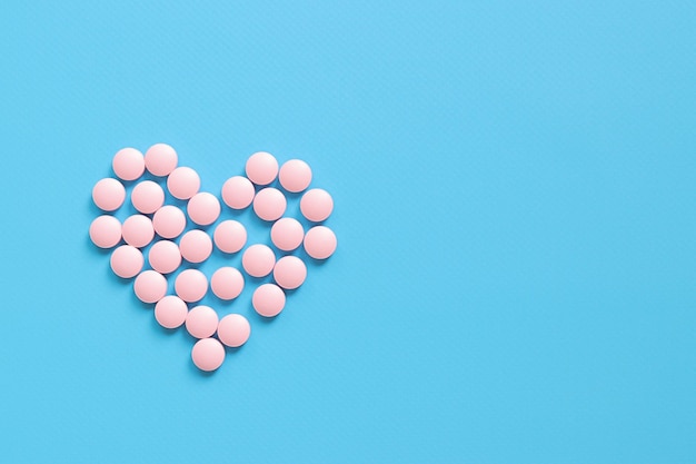 Coração forrado com pílulas cor-de-rosa em um fundo azul de borracha vista superior conceito de saúde