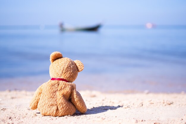 Coração partido ou conceito de solidão. urso de pelúcia sozinho sentado na praia de areia com mar azul. símbolo de abandono, tristeza, solitário, desapontado.