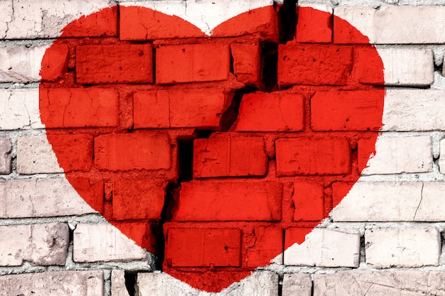 Coração partido vermelho na parede de tijolo com grande fenda no meio. Conceito de amor quebrado