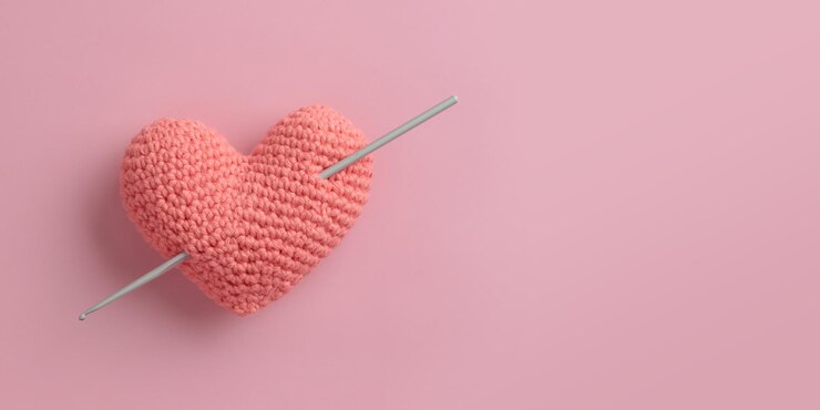 Coração rosa amigurumi de crochê com agulha de crochê em um banner de dia dos namorados de fundo rosa