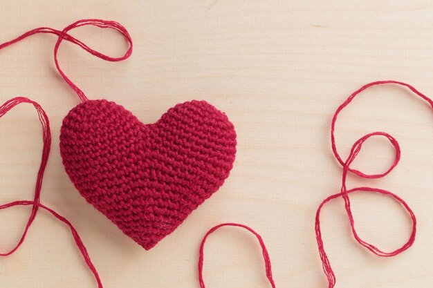 Coração rosa amigurumi de crochê em um fundo de madeira com um fio de dia dos namorados