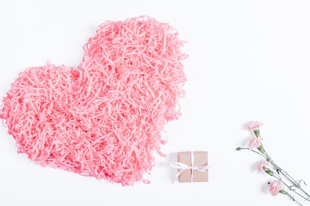 Coração rosa decorativa, caixa pequena com um presente e fita e flores em uma superfície branca