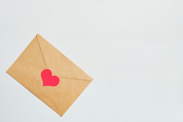 Coração vermelho com um envelope de ofício em um fundo branco de madeira. Copie o espaço.