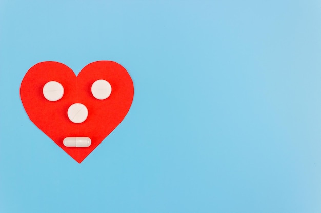 Coração vermelho com um rosto feito de pílulas em um fundo azul. O conceito de prevenção e tratamento de doenças cardíacas. Copie o espaço.