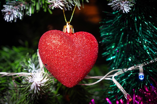 Coração vermelho de enfeites de Natal na árvore de Natal em fundo bokeh brilhante com luzes cintilantes Cartão de Feliz Natal Tema de férias de inverno Feliz Ano Novo