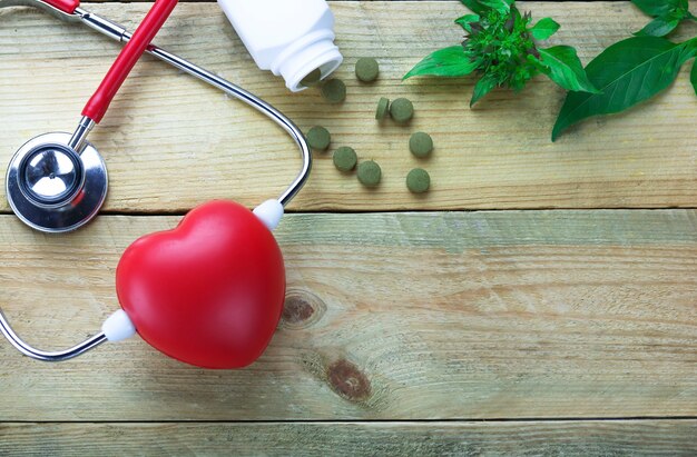 coração vermelho e estetoscópio com drogas à base de plantas na mesa de madeira