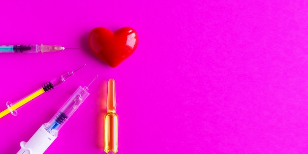 Coração volumétrico com seringas em um fundo rosa. O conceito de apoiar pacientes com doenças cardíacas.