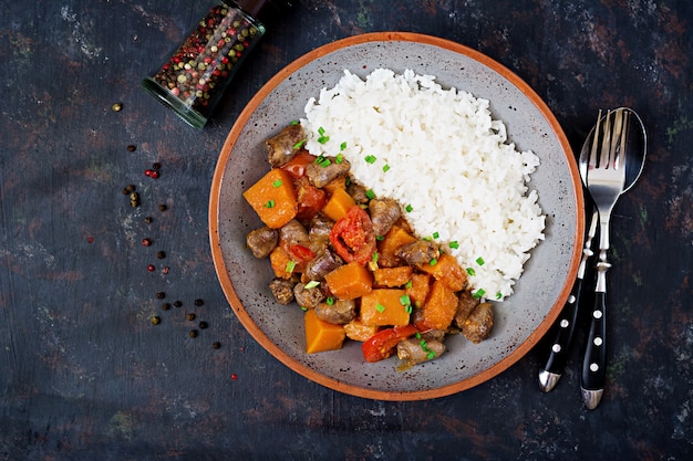 Corações de frango com abóbora e tomate em molho de tomate. O enfeite é servido com arroz cozido. Postura plana. Vista do topo.