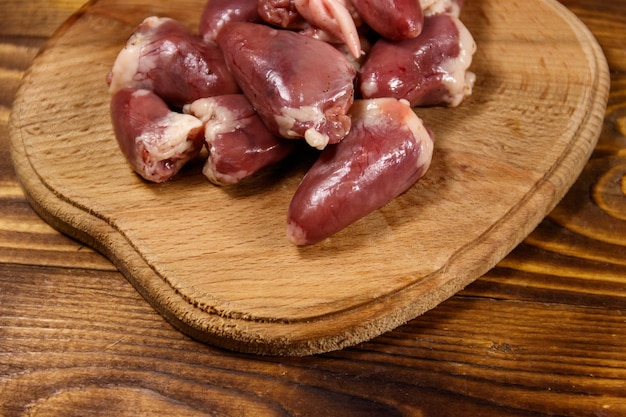 Corações de frango cru na tábua na mesa de madeira