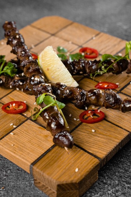 Corações de frango grelhado com limão no espeto de madeira, decorado com pimenta, coentro e gergelim na superfície cinza.